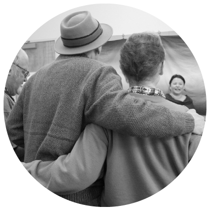 Male with hat and female hug while looking towards the front of a room
