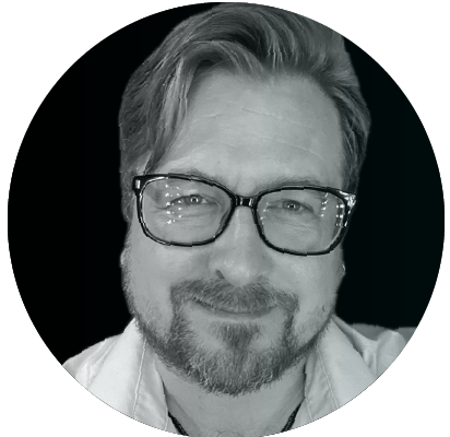 greyscale image of a man with a goatee wearing glasses.